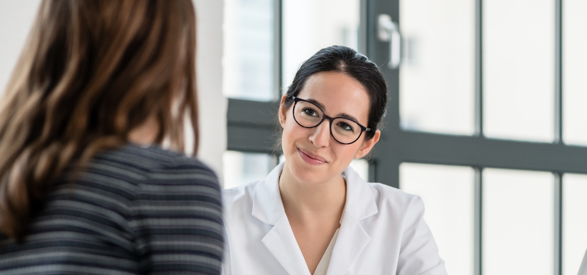Female physician listening to her patient during consultation while sitting down in the office of a modern medical center jpg